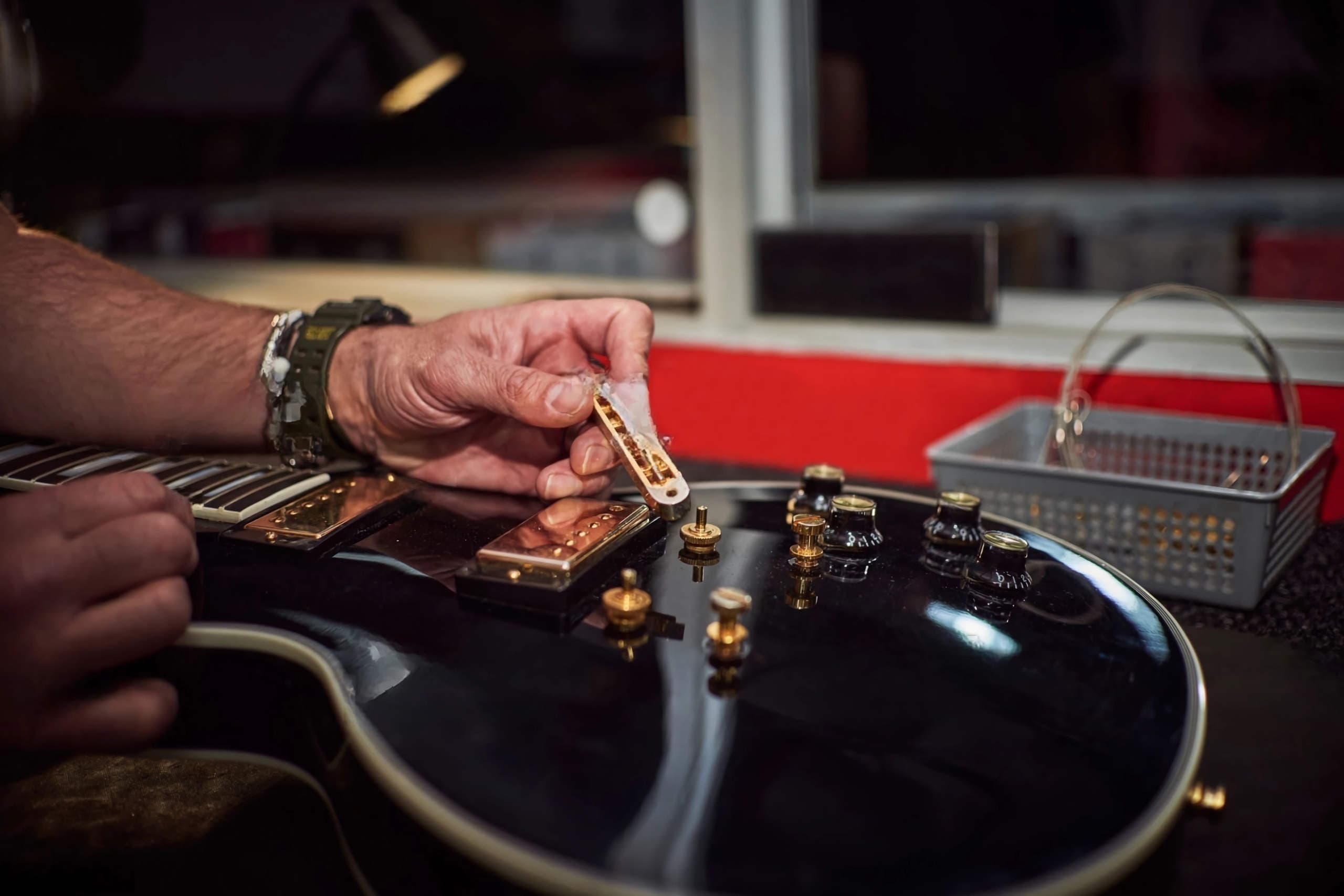 Black Les Paul with gold hardware on a luthier's workbench under warm lamp light.