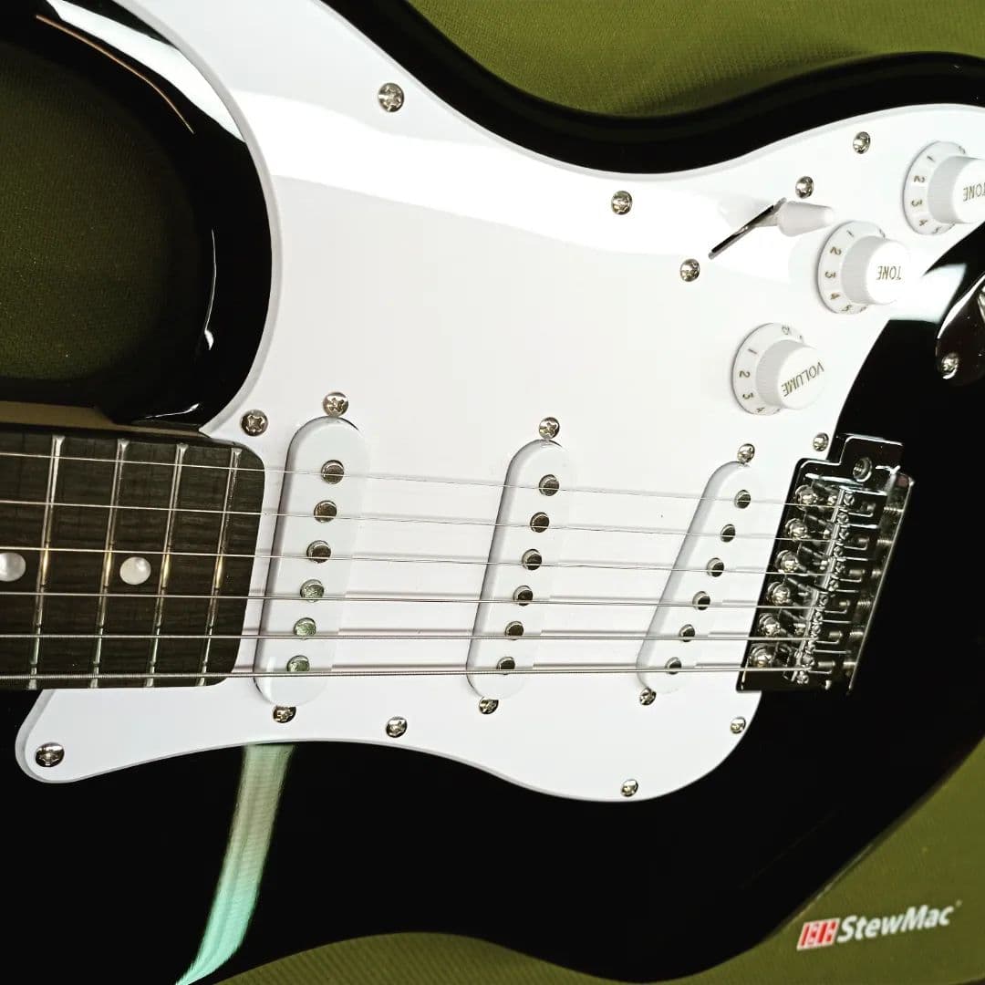 Black-finish Stratocaster with white pickguard and three single-coil pickups, set up flat on the bench.