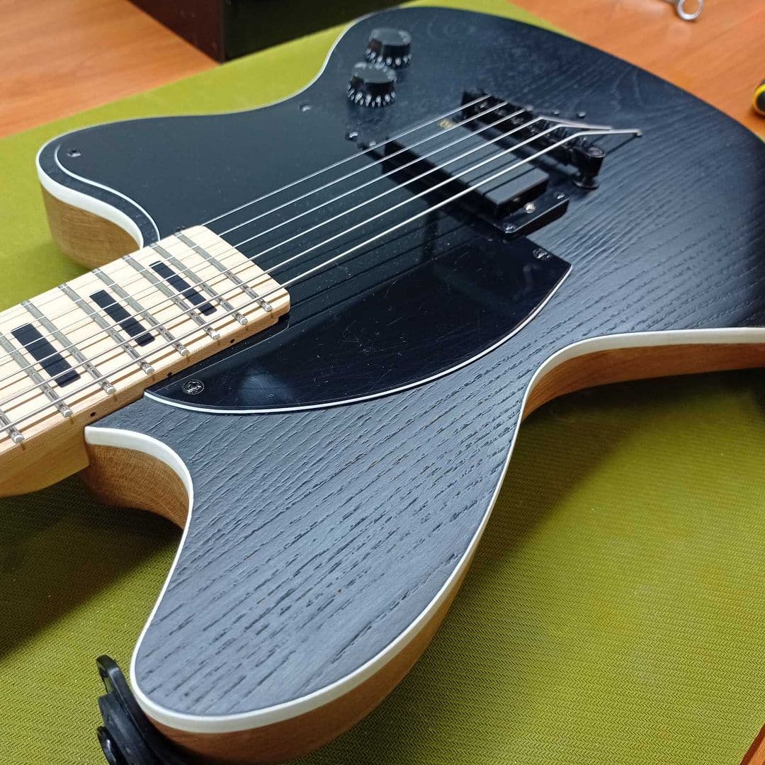 Black open-pore ash offset guitar with a maple neck and cream body binding, fresh from a finish job.