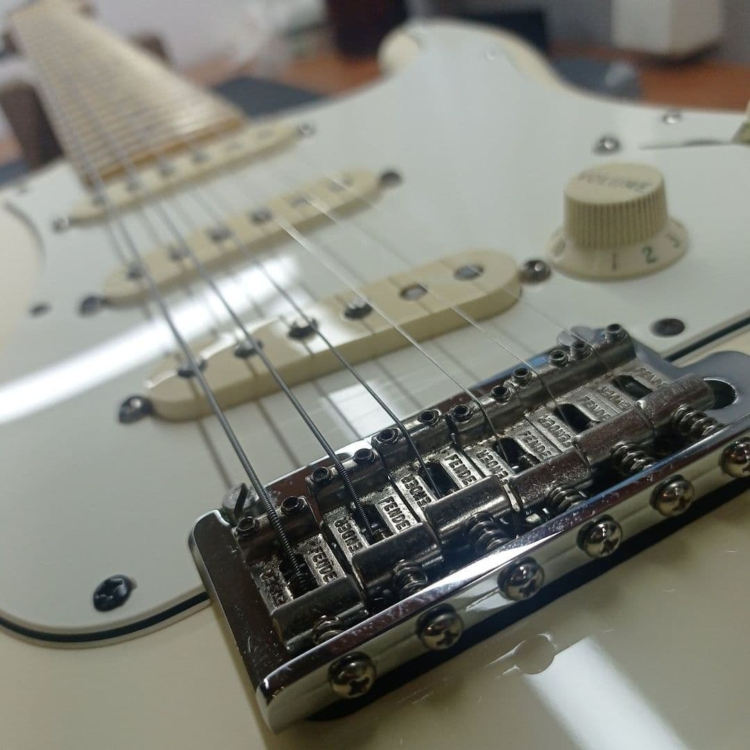Close-up of a white Stratocaster's chrome tremolo bridge and saddles during string setup and intonation.