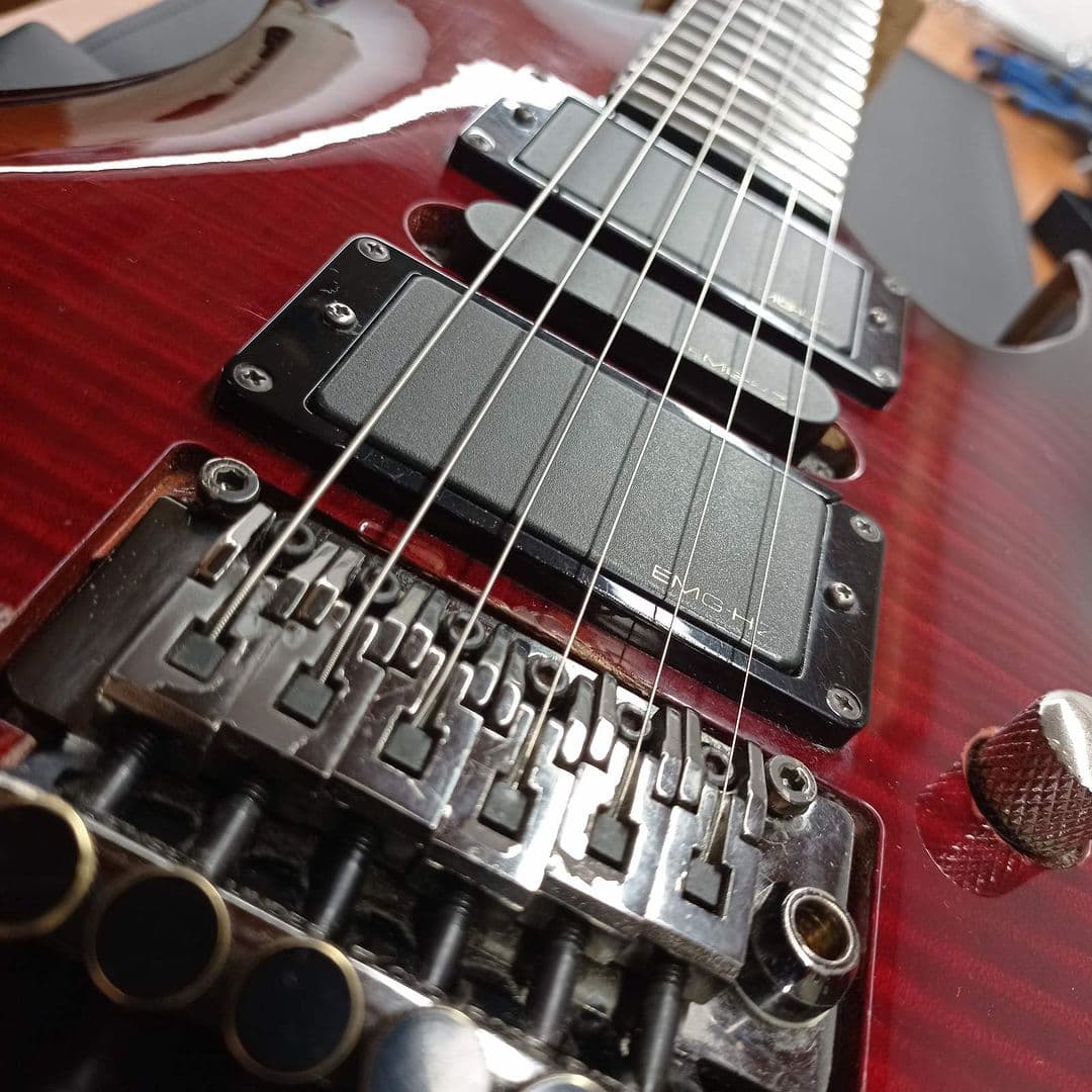 Detail of a deep-red electric guitar with EMG humbuckers and a Floyd Rose tremolo on the bench.