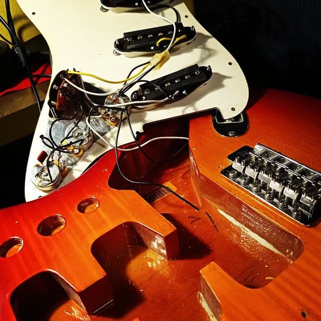 Exposed body cavity of a sunburst Stratocaster showing the wiring and pickups during an electronics job.